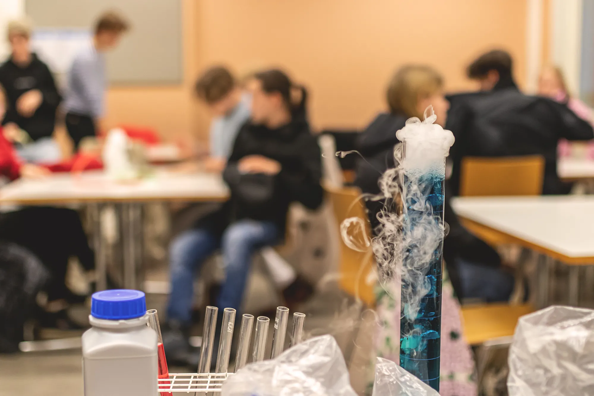 Luokkahuoneessa nuoria istumassa, etuosassa höyryävä koeputki.